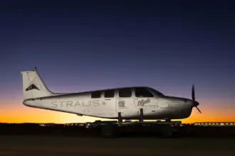 A silver Stralis aircraft at sunset. A line of orange lights illuminates the plane beneath a dark blue sky.