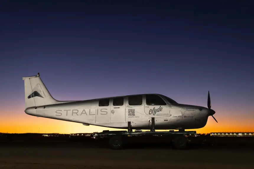 A silver Stralis aircraft at sunset. A line of orange lights illuminates the plane beneath a dark blue sky.