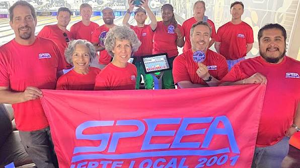 A group of SPEEA members dressed in red and stood behind a red and blue SPEEA banner.