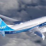 A blue and white Boeing 737 jet flying over a cloudy sky.