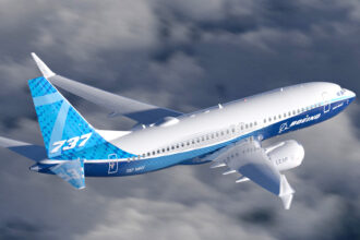 A blue and white Boeing 737 jet flying over a cloudy sky.