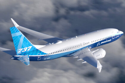A blue and white Boeing 737 jet flying over a cloudy sky.