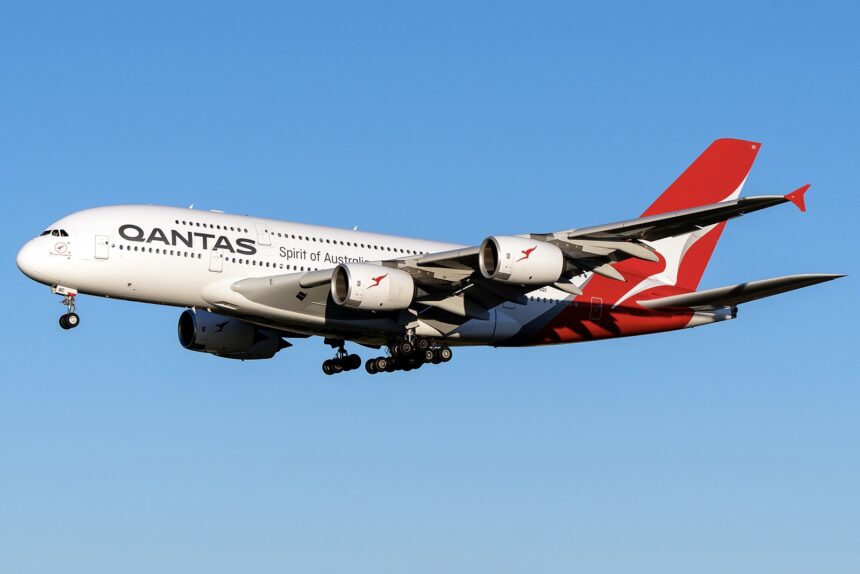 A red and white Airbus A380 jet in the livery of Qantas Airways. The jet is flying in front of a clear blue sky.