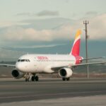 An Iberia A320 sitting on tarmac with a cloudy sky backdrop.