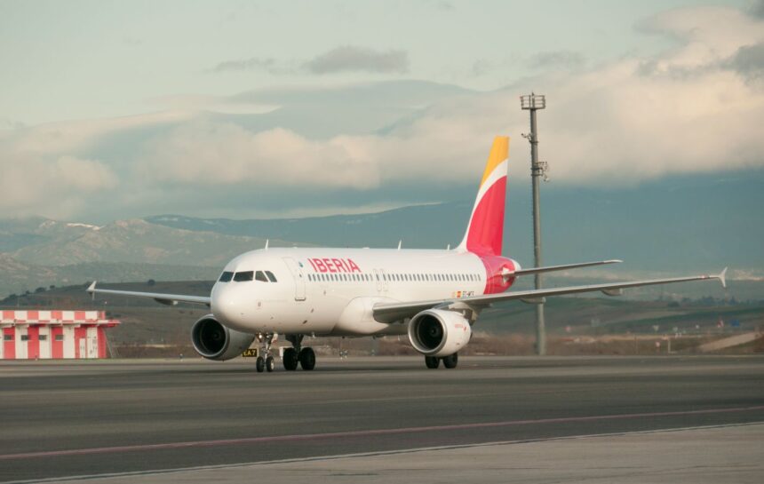 An Iberia A320 sitting on tarmac with a cloudy sky backdrop.