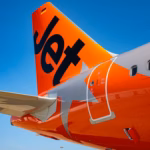 Bold orange rear of a Jetstar A321, featuring the company logo. The plane is against a sunny blue sky background.