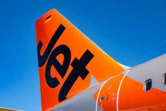 Bold orange rear of a Jetstar A321, featuring the company logo. The plane is against a sunny blue sky background.