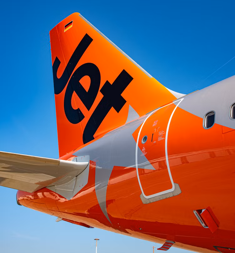 Bold orange rear of a Jetstar A321, featuring the company logo. The plane is against a sunny blue sky background.