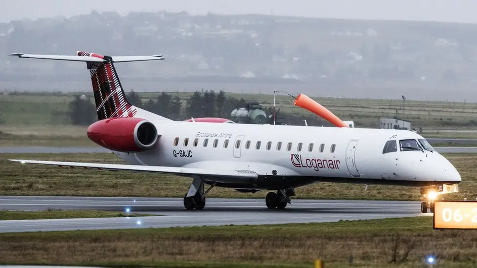 A Loganair aircraft pictured on an airport runny in grey weather.