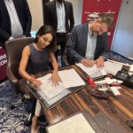 CEO's of Noemi Aerospace and SkyHop Aviation make sea plane deal. Both are sat down on a desk signing an agreement. They both look happy about the new achievement.
