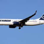 A TAROM Boeing 737-800 aircraft flying through the blue sky.