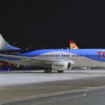 A TUI aircraft parked on the tarmac of an airport. A dark night sky is the background and the lights of various buildings and vehicles can be seen just behind the plane.