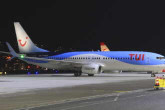 A TUI aircraft parked on the tarmac of an airport. A dark night sky is the background and the lights of various buildings and vehicles can be seen just behind the plane.