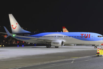 A TUI aircraft parked on the tarmac of an airport. A dark night sky is the background and the lights of various buildings and vehicles can be seen just behind the plane.
