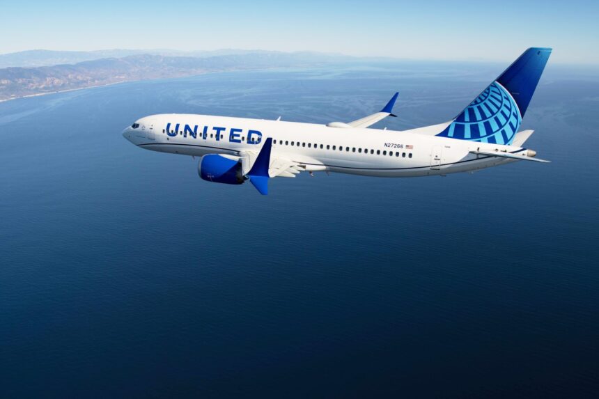 A United Airlines Boeing 737 Max-8 pictured flying over a body of open water against blue skies.
