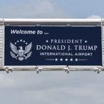 A navy road sign picture on the way into Palm Beach County's Airport, reading "Welcome to... President Donald J. Trump International Airport."