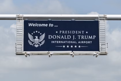 A navy road sign picture on the way into Palm Beach County's Airport, reading "Welcome to... President Donald J. Trump International Airport."