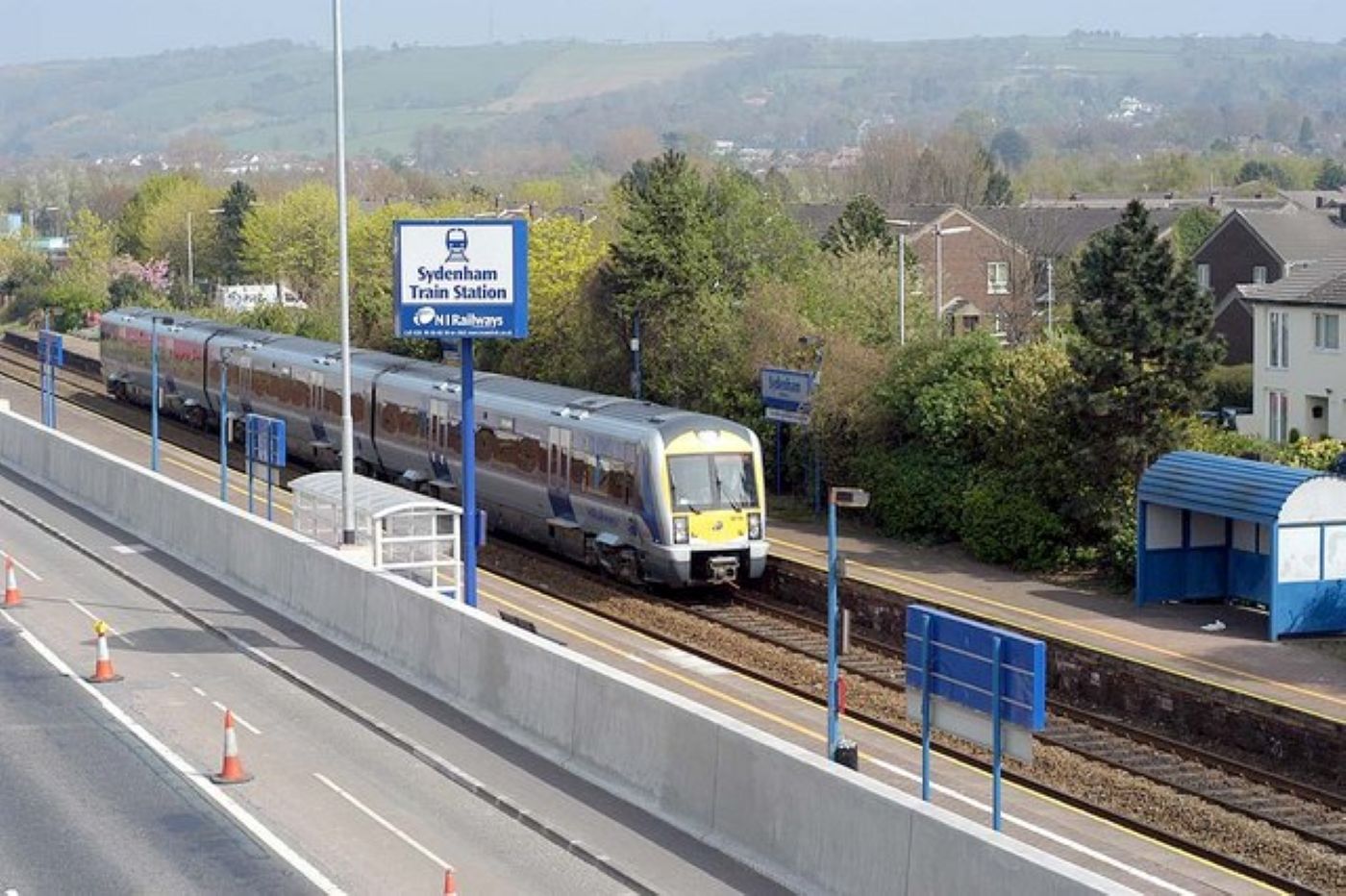 Aerial view of Belfast railway train moving through tracks with trees around it and a view of the city