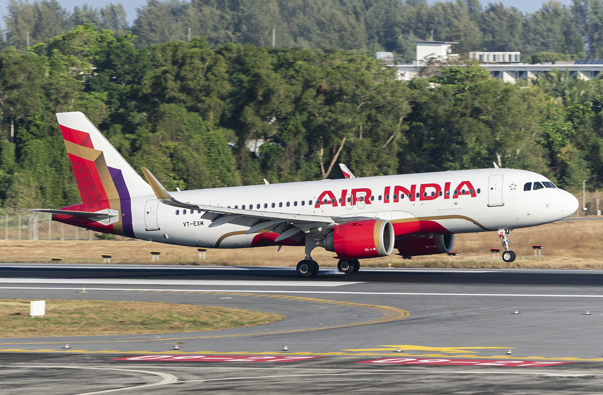 An Air India A320 landing on a concrete runway with trees seen in the background.
