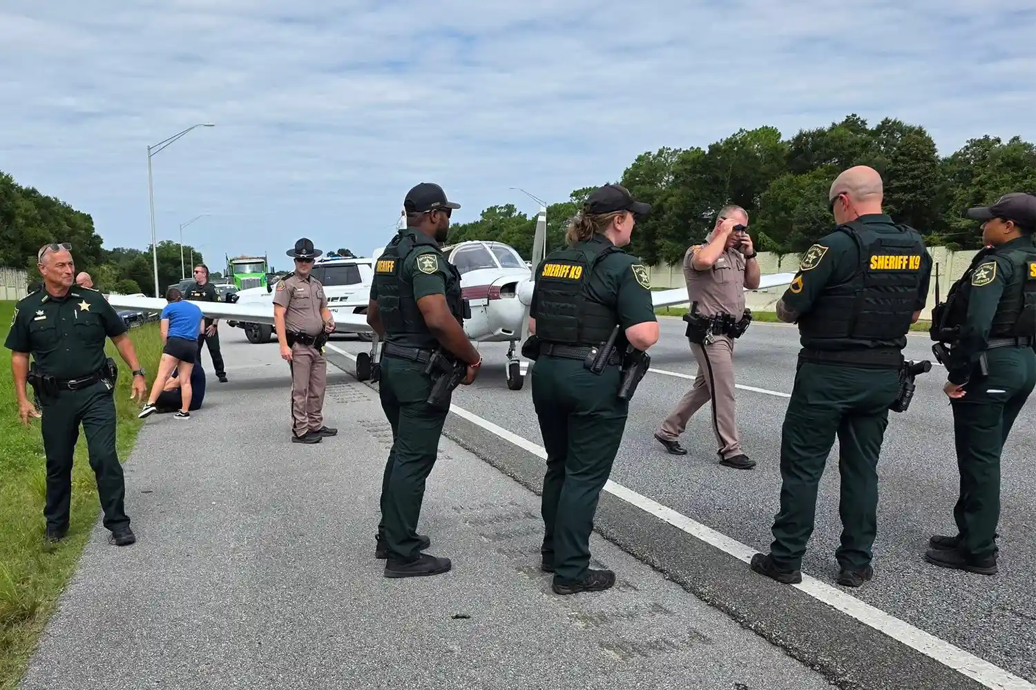 The Piper PA-28 on the right side of the highway after its emergency landing surrounded by police.
