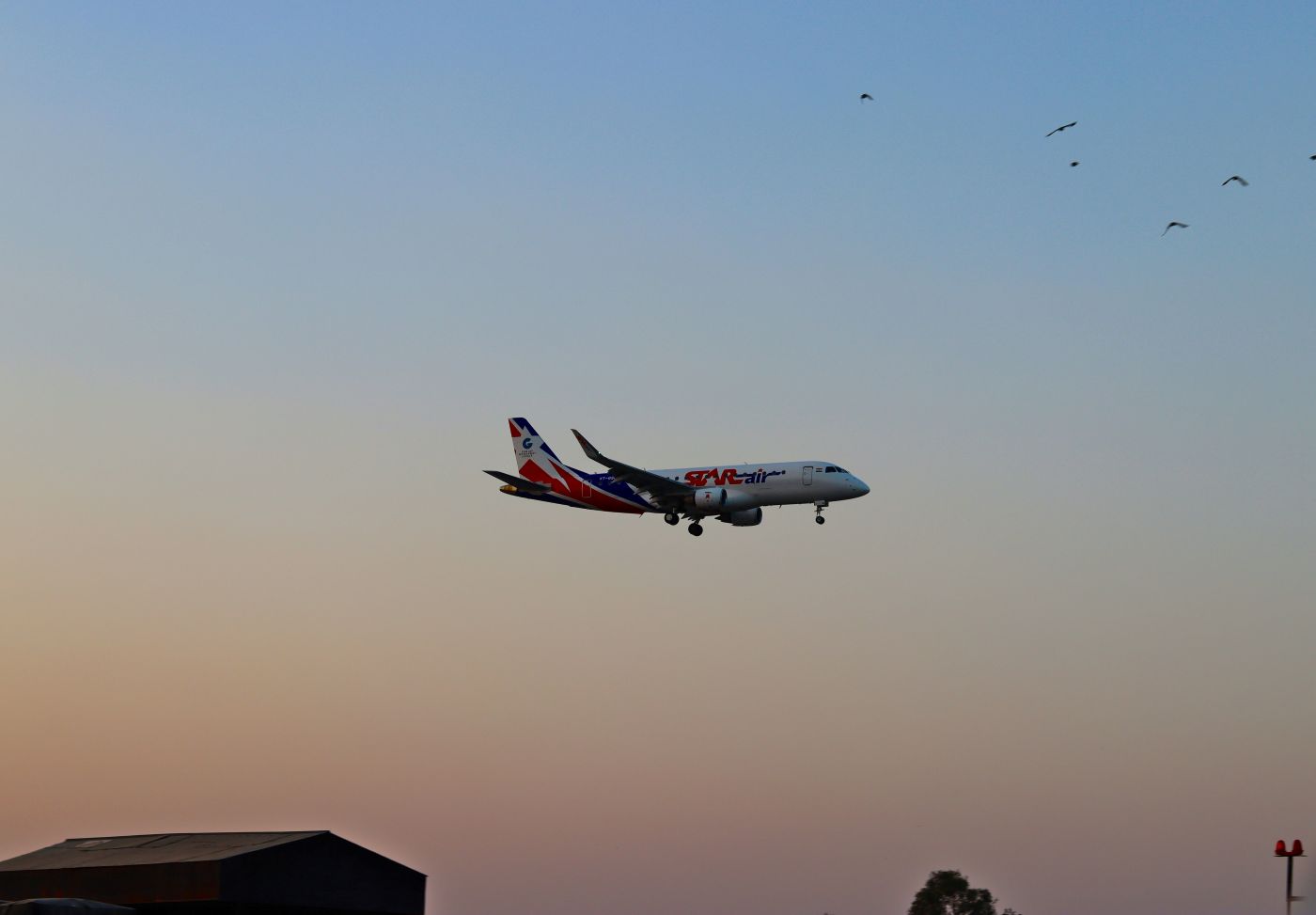 Embraer E175 Aircraft in the middle of the sky with a blue and red sunset in the background