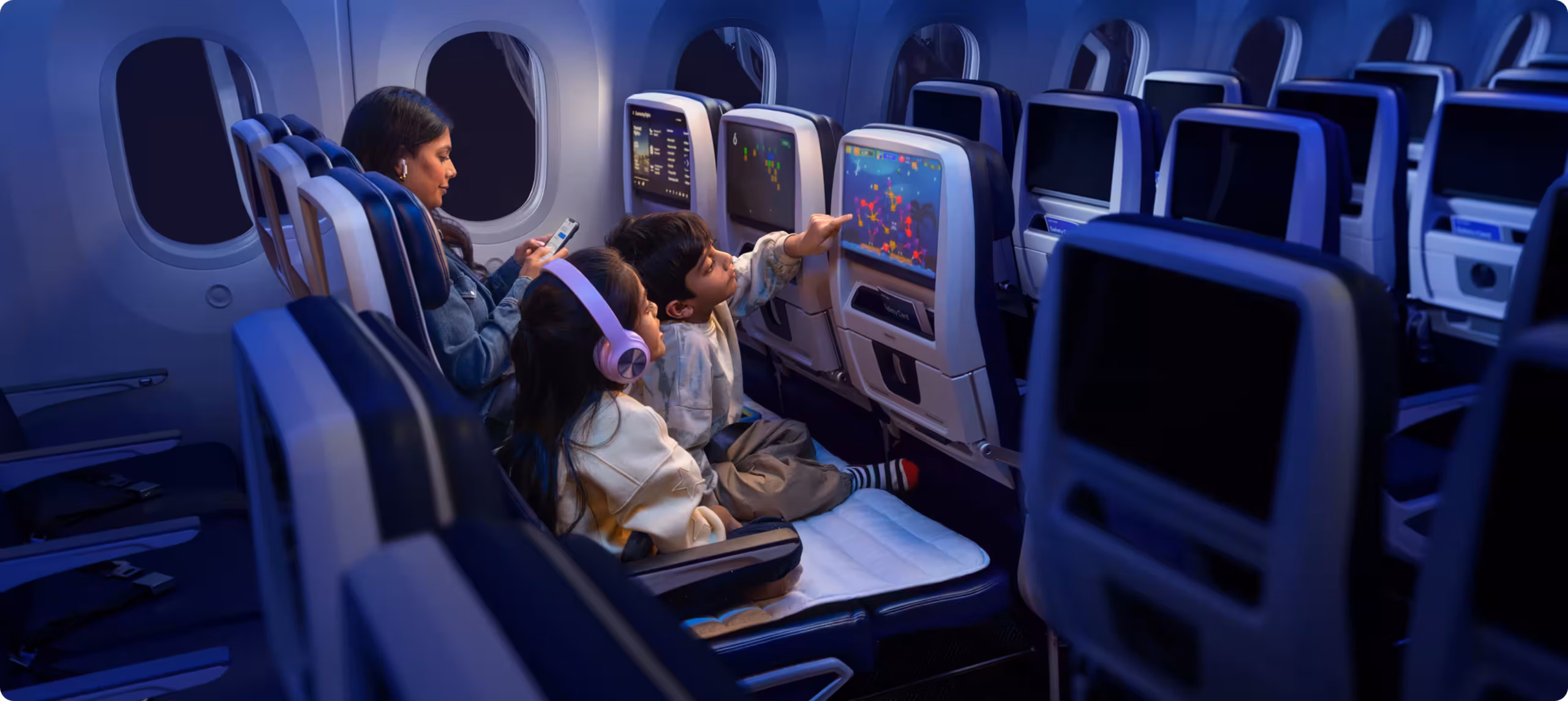 Family of three – a mother and two children – sat in United Airlines' Relax Row. The children are using the large seatback screen.