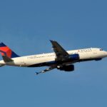 A delta Airbus with a blue tail flying midair with a clear blue sky background.
