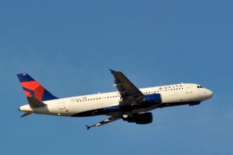 A delta Airbus with a blue tail flying midair with a clear blue sky background.