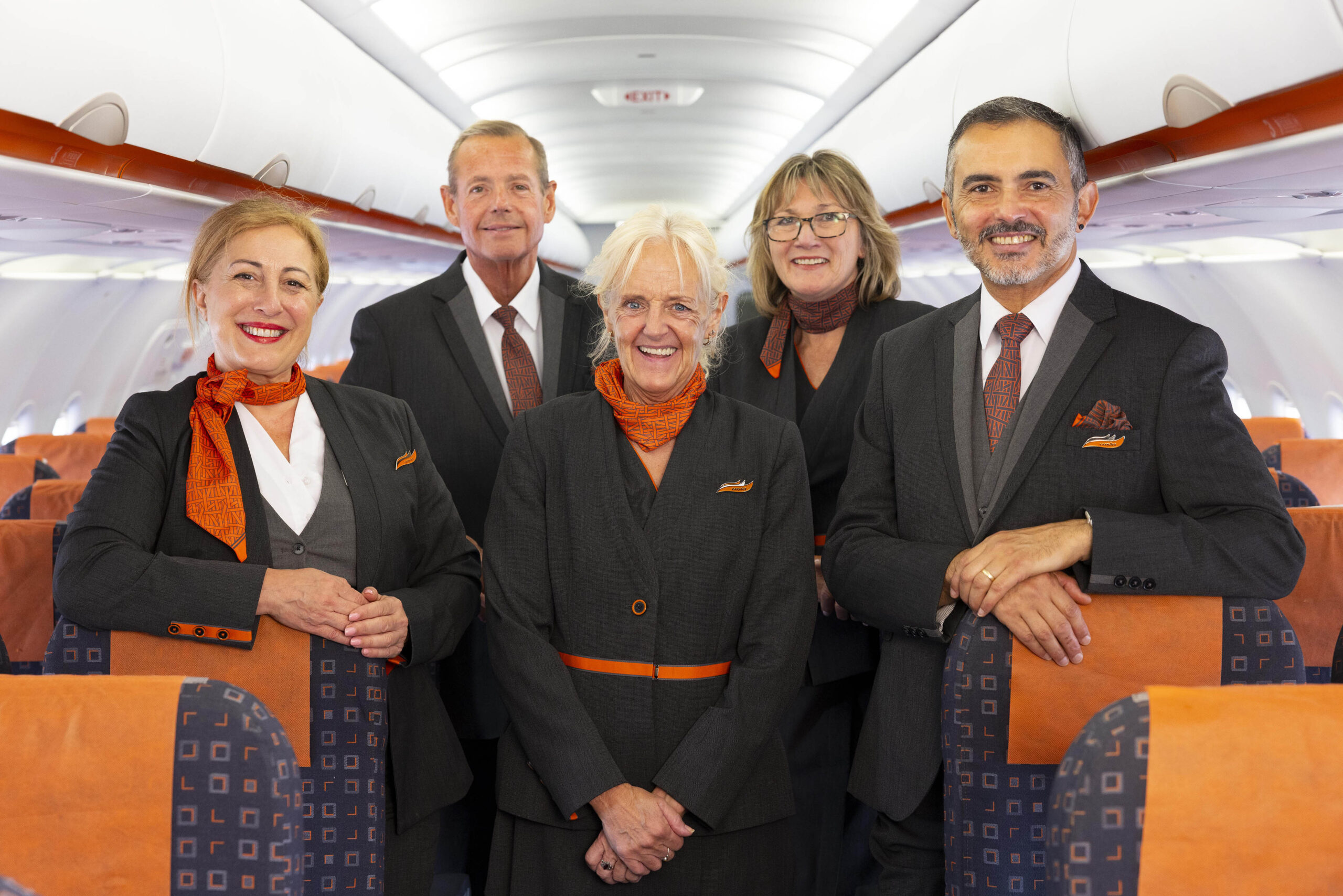 Image shows five smiling easyJet cabin crew inside a well-lit aircraft