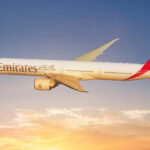 Photograph depicting Emirates Boeing 777 aircraft cruising at altitude above the clouds at sunset.
