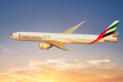 Photograph depicting Emirates Boeing 777 aircraft cruising at altitude above the clouds at sunset.