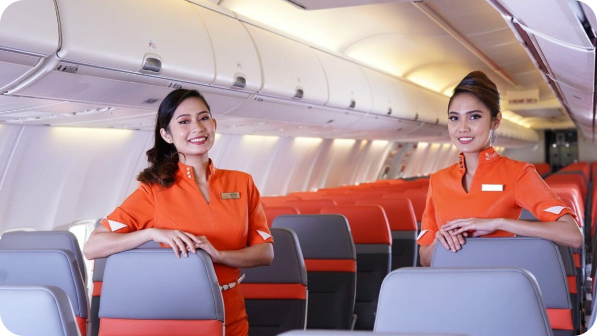 Two female cabin crew members, in orange uniform, smiling for a photo inside a Firefly aircraft.
