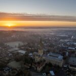 Photograph of Norwich city centre from above at sunset or sunrise, which can be seen on the horizon.