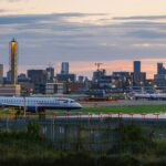 British Airways aircraft on an airport taxiway at sunset, with multiple parked planes and a city skyline in the background
