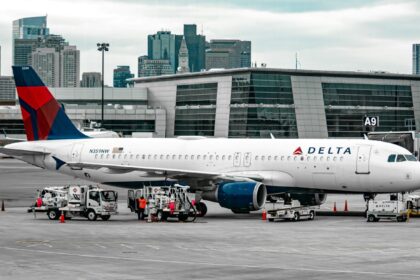 A Delta Air lines aircraft parked on tarmac with a cloudy but bright sky background and a terminal in the background.