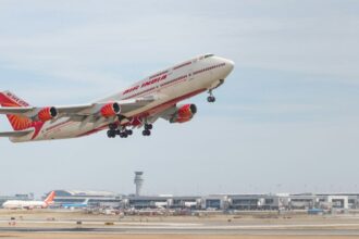 Air India double decker aircraft midair in a take off position it has a red tail and wing tips and the tarmac can be seen in the horizon with a cloudy sky
