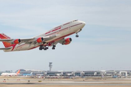 Air India double decker aircraft midair in a take off position it has a red tail and wing tips and the tarmac can be seen in the horizon with a cloudy sky