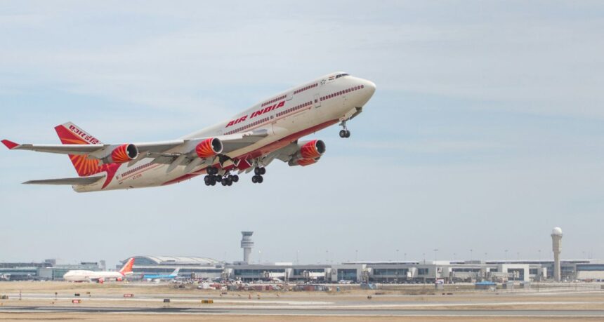 Air India double decker aircraft midair in a take off position it has a red tail and wing tips and the tarmac can be seen in the horizon with a cloudy sky