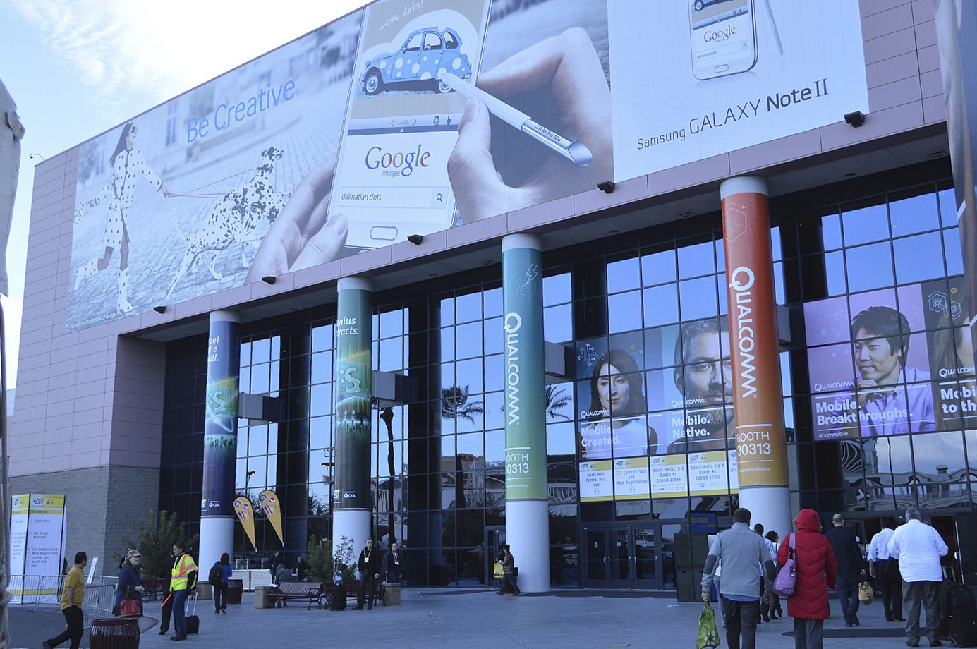 The exterior of Las Vegas Convention Center can be seen with people walking into the building and large adverts being displayed along the front of the center.