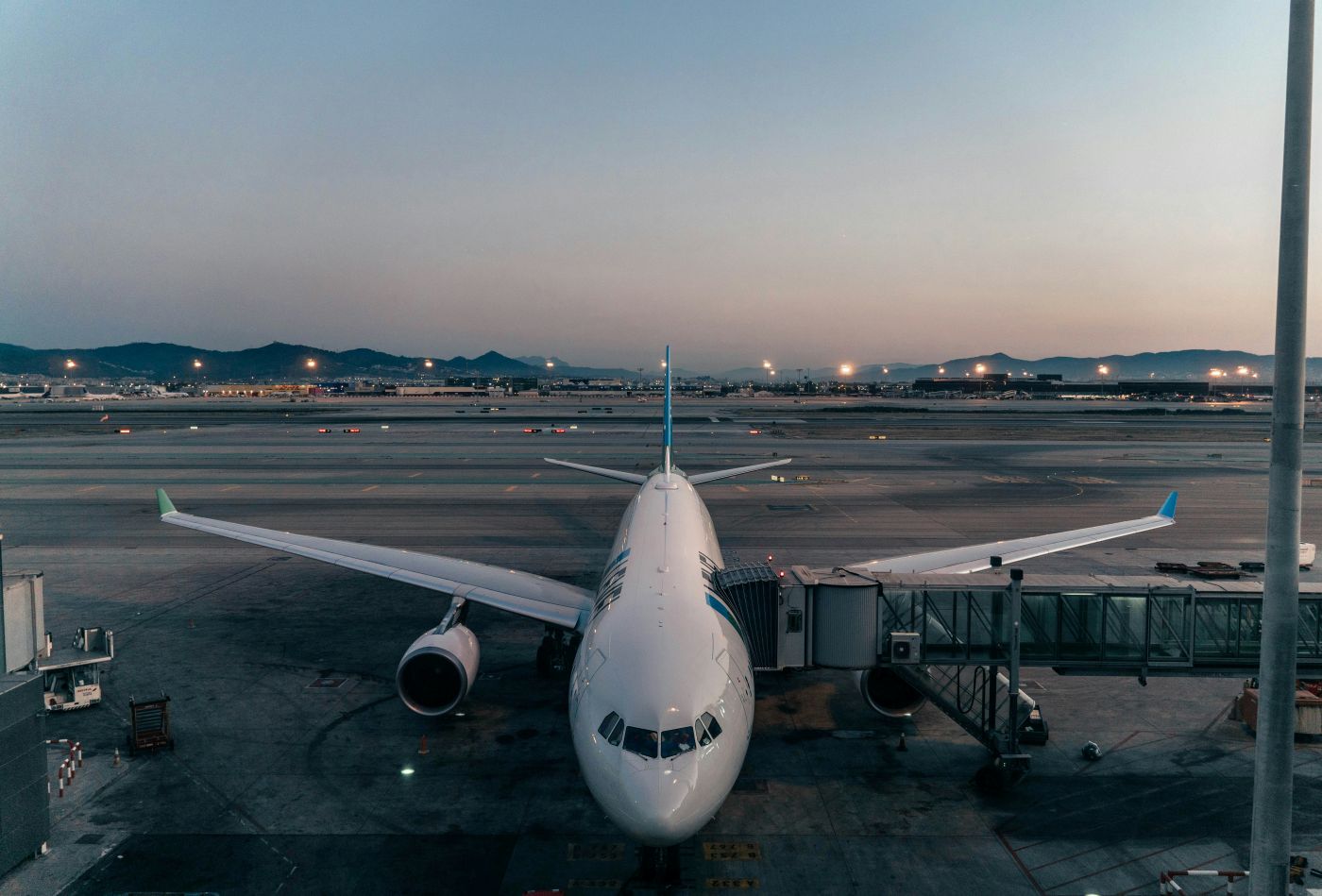 An Airbus aircraft at landing with a passenger tunnel attached to it and a sunset in the background
