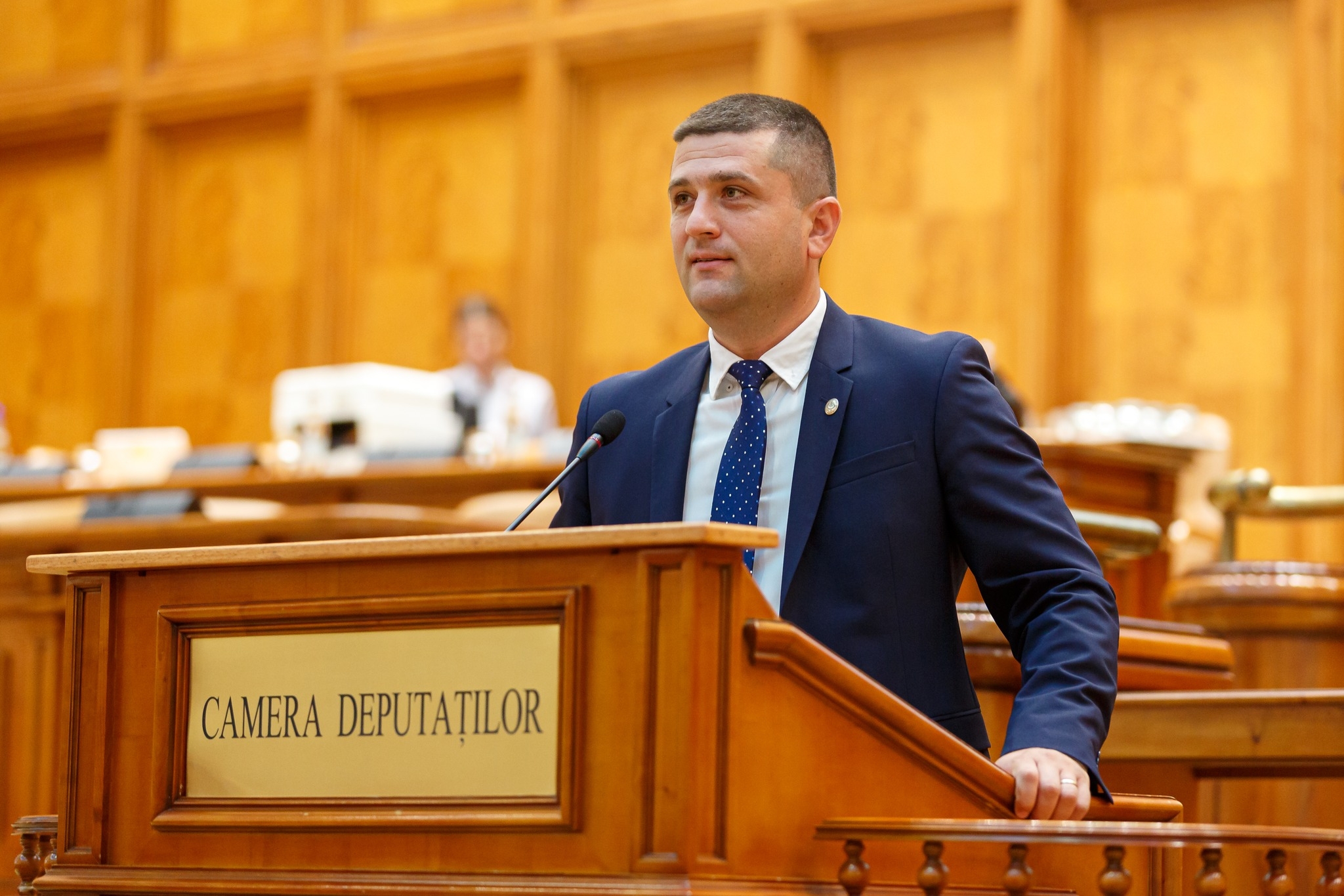 Radu Miruta speaking at the Chamber of Deputies stand; he is dressed in a suit and tie looking at the plenary.