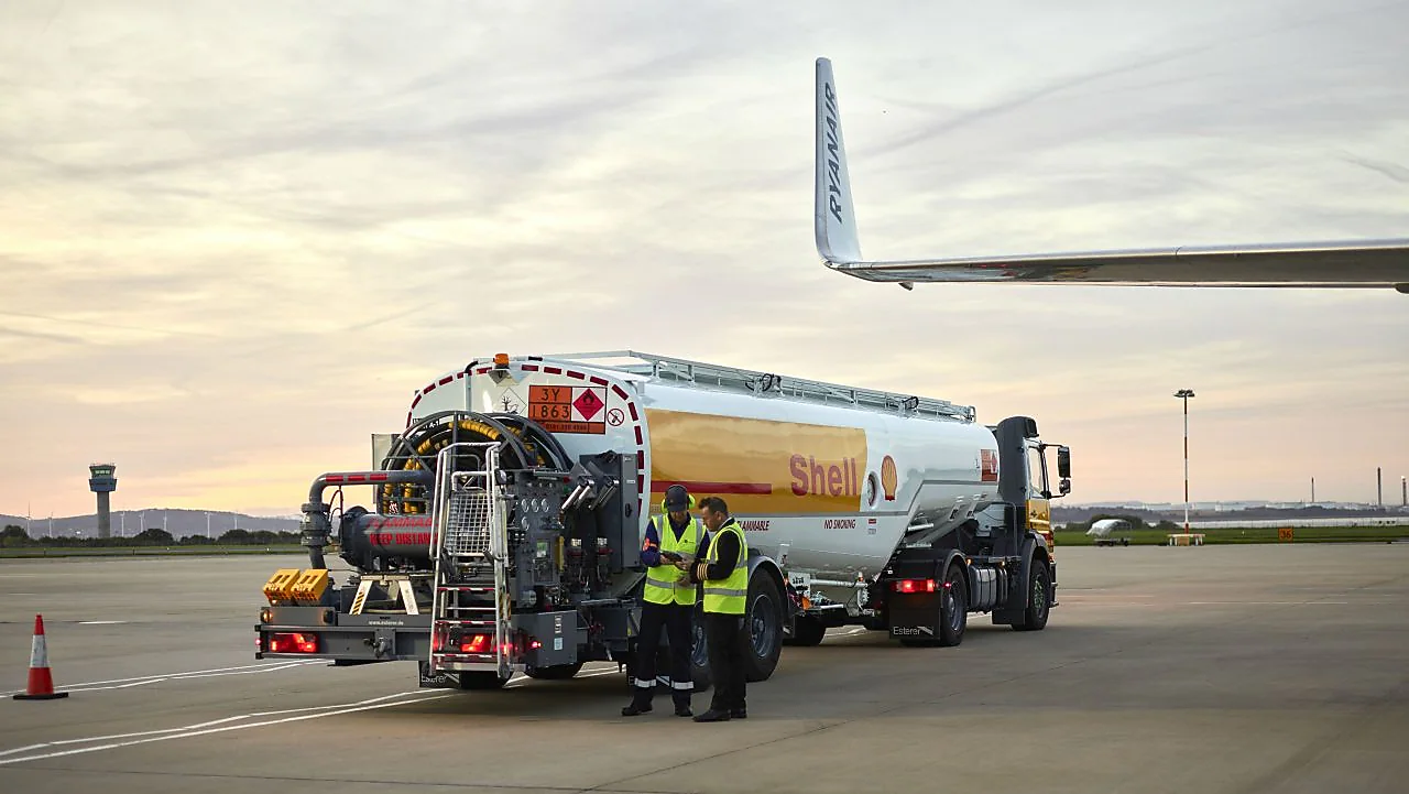 A Shell aviation fuel tank on a runway featuring 2 people dressed in neon vests