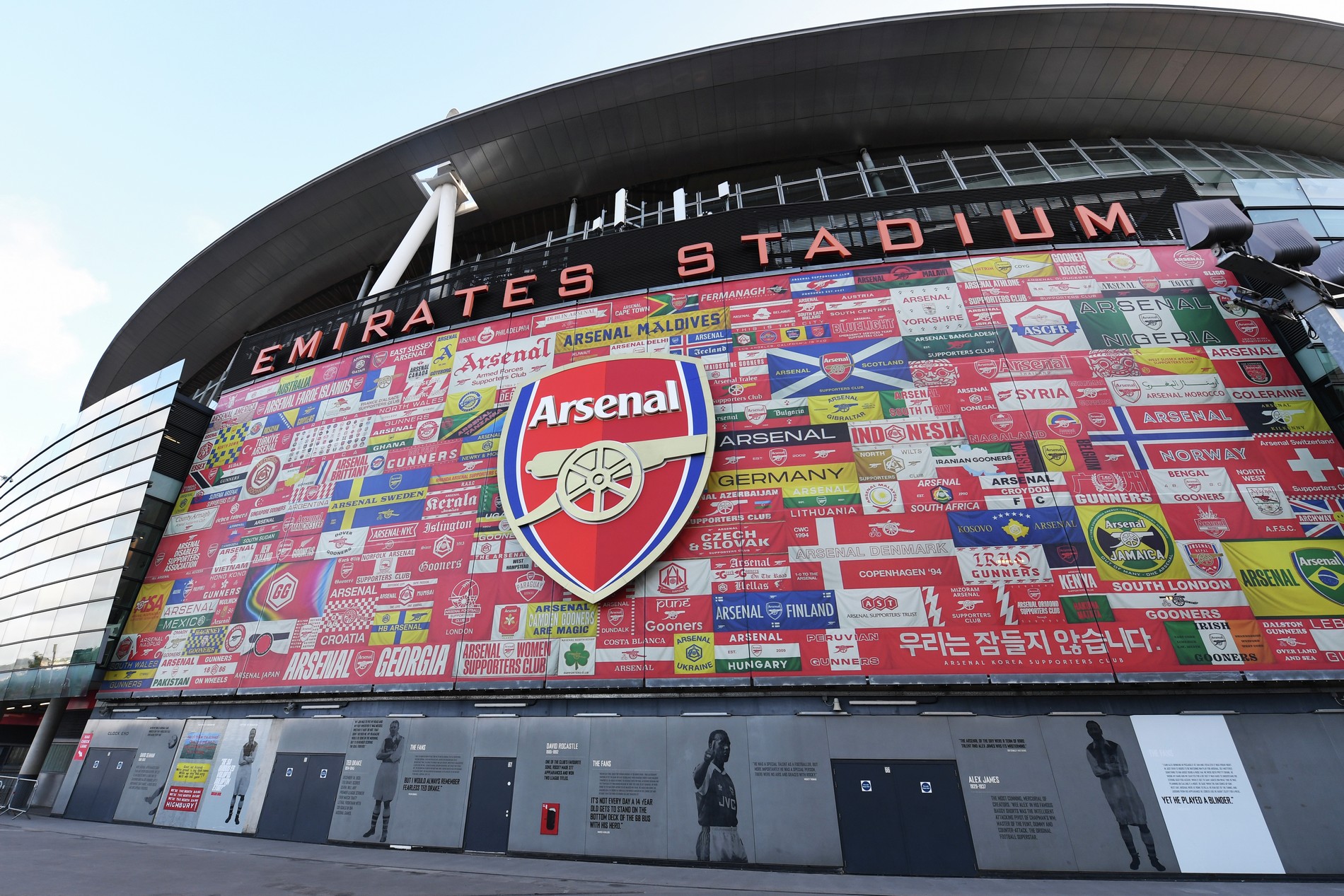 Photograph depicting the exterior of Emirates stadium covered in flags from around the world and featuring the Arsenal logo.