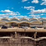 A street view of Ronald Reagan Washington National Airport, with a busy road of cars driving in front of the airport and a clear blue sky.