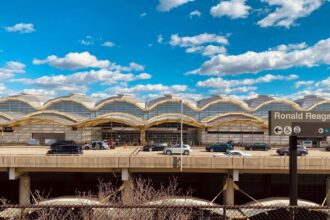 A street view of Ronald Reagan Washington National Airport, with a busy road of cars driving in front of the airport and a clear blue sky.