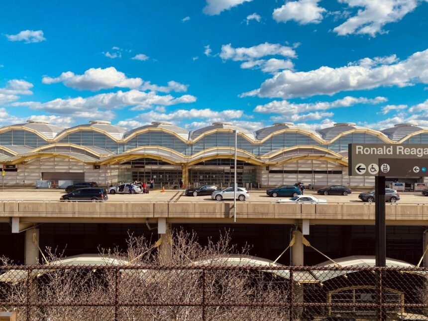 A street view of Ronald Reagan Washington National Airport, with a busy road of cars driving in front of the airport and a clear blue sky.