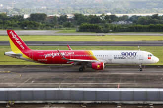A VietJetAir A321 plane sat on a concrete runway with green grass and foliage in the background.