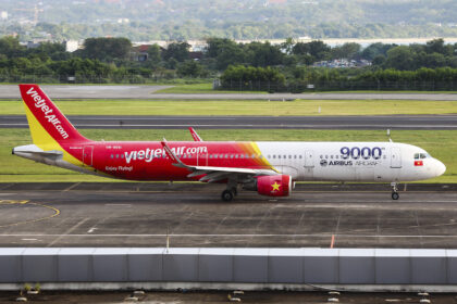 A VietJetAir A321 plane sat on a concrete runway with green grass and foliage in the background.