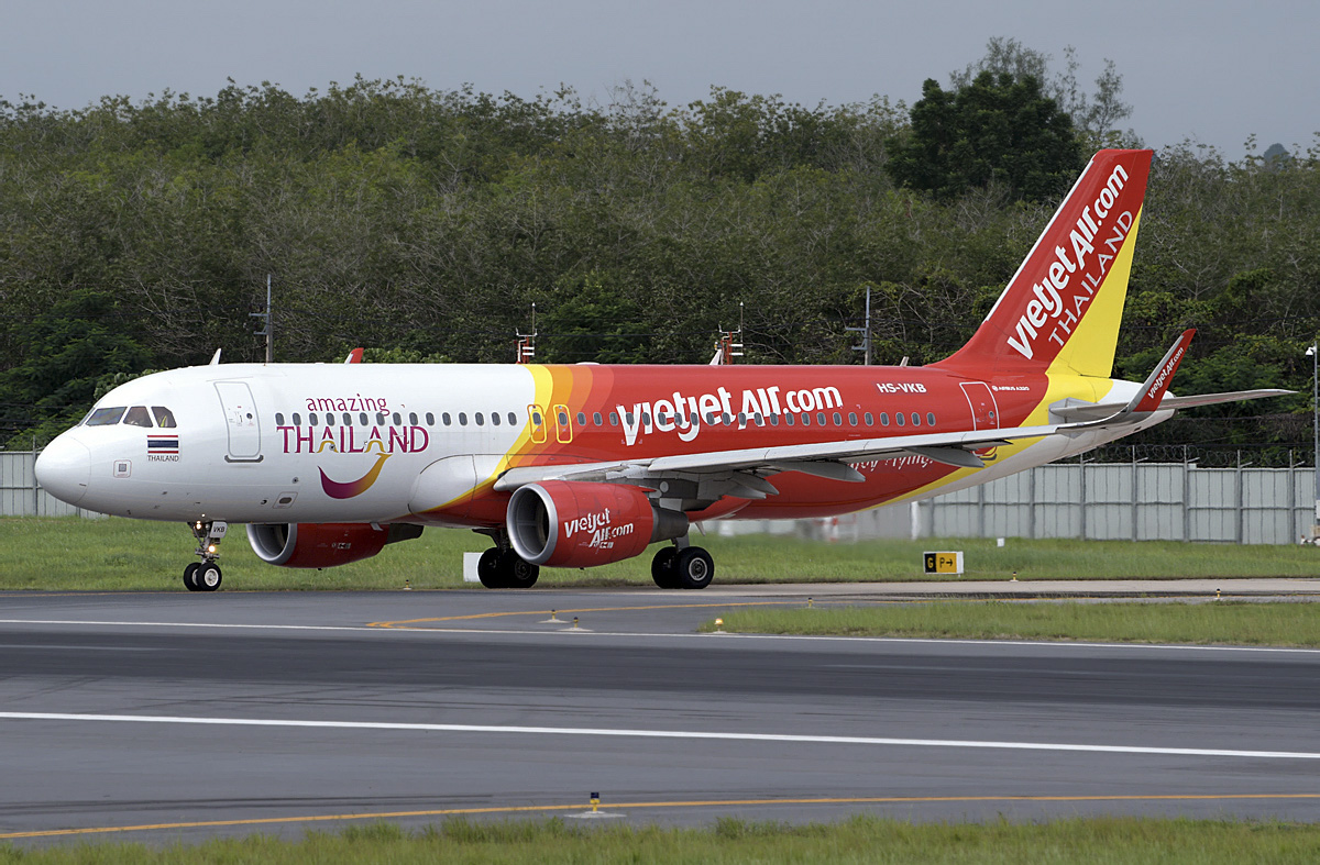 A Thai VietJetAir Airbus A320 landed on a runway with green trees in the background.