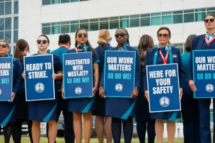 A row of WestJet flight attendants standing on a picket line with signs reading 'Our work matters, so do we!', 'Ready to strike.', and 'Frustrated with WestJet? So are we.'
